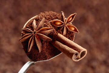 Spoon of ground coffee with anise and cinnamon on the background of coffee beans.