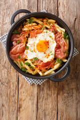 Spanish cuisine fried egg with fries and ham close-up in a plate on the table. vertical top view from above