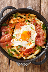 Huevos rotos con jamon fried egg with fries and ham close-up in a pan on the table. Vertical top view from above