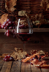 Wine, grapes and dried up vine leaves on a old wooden table.