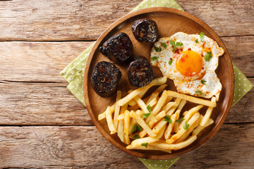 Huevos Rotos with fried potatoes and black pudding close-up in a plate on the table. Horizontal top...