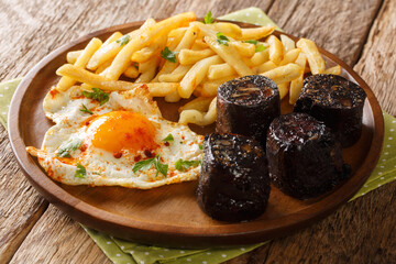 Huevos Rotos with fried potatoes and black pudding close-up in a plate. Horizontal
