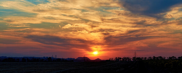 Obraz premium sunset with multicolored clouds in the sky in the summer field. panorama banner