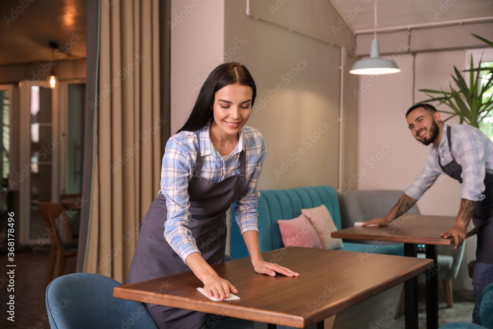 Sticker Young waitress cleaning table in restaurant