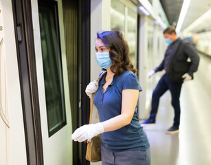 Portrait of young focused woman in medical facial mask and latex gloves landing in subway car. Concept of health protection during coronavirus pandemic