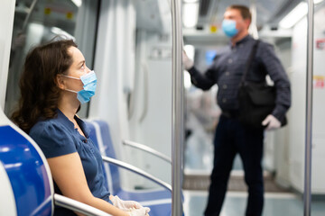 Young brunette in medical face mask and protective gloves riding in modern subway car. Concept of...