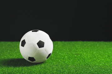 Fototapeta premium White and black soccer ball on green artificial turf with dark background, sports and recreation concept, the classic football design with its hexagonal pattern is clearly visible against a dark