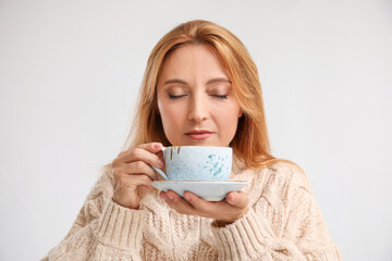Beautiful woman with cup of tea on light background