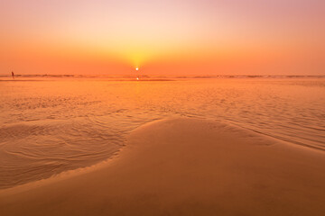 A colorful sunset or sunrise on the seaside with a sandy beach with impurities of volcanic ash. Mandrem, Goa, India.