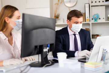 Fototapeta premium Portrait of busy entrepreneur in medical face mask and latex gloves working with female coworker in office. Concept of precautions and social distancing in coronavirus pandemic..