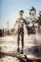 Fototapeta premium The silhouette of a boy is seen behind the drops of water in the fountain
