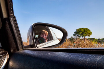 Car Mirror and reflection of traveller photographer and sky in it.