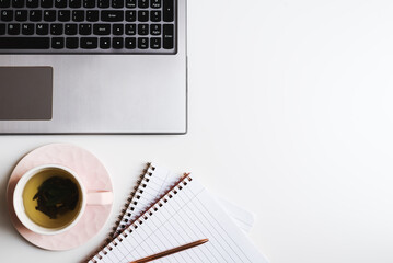 Laptop computer, green tea in a pink cup, notebooks with clean pages and metal pen on white table....