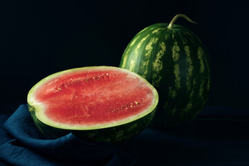 One whole ripe watermelon and sliced one on dark blue wooden table.