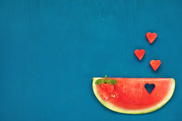Watermelon slice with cut out hearts and mint leaf on blue wooden background. Flat lay. Space for text.