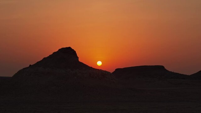 Wide shot of the sun during a sunset with silhouetted hills on left and right of the frame.