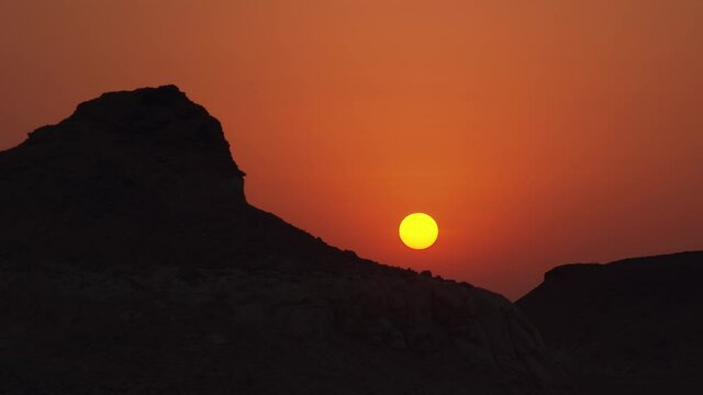 Close up of the sun during a sunset with silhouetted hills on left and right of the frame.