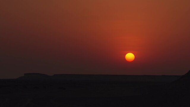 Medium shot of a sunset with rocky hills in the foreground in Zekreet Desert in Qatar.