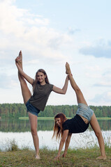 two girls do gymnastic exercises outdoor in a picturesque place by the river and having fun