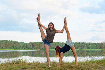 Fototapeta na wymiar two girls do gymnastic exercises outdoor in a picturesque place by the river and having fun