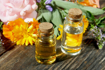 Selection of  glass aromatherapy essential oil bottles, with herbs and flowers in the background