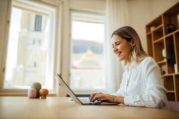 Side view portrait of a cheerful young woman using laptop at home office.