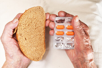 View from above. In her hands an old grandmother of 90 years holds bread in one hand and pills in...