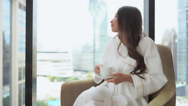 Pretty Asian Female Drinking Morning Coffe In Bathrobe By Window Of Family Home