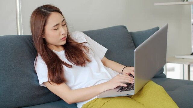 Asian female tiredy awning while doing work from home during Covid-19 pandemic time. Exhausted Asian woman feeling sleepy while working on her laptop.