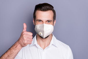 Close-up portrait of his he attractive healthy guy wearing safety n95 respirator mask showing thumbup stop influenza pandemia medicine air pollution smog solution isolated gray color background
