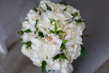 Gold wedding rings and a bunch of white hydrangeas on the sofa. Wedding still life. Selective focus.