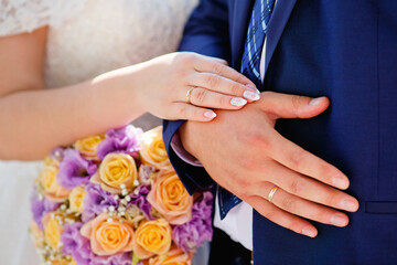 Hands of the bride and groom. Bride and groom holding hands at a wedding ceremony. Wedding rings on the hands of the newlyweds. Hands of the newlyweds on the background of a wedding bouquet