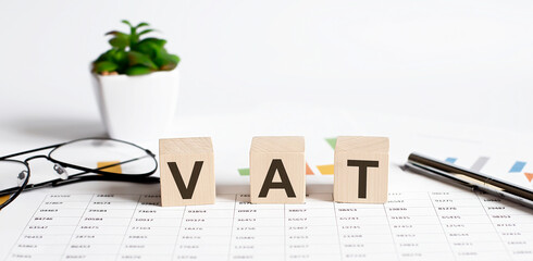 VAT word concept written on wooden blocks, cubes on a light table with flower ,pen and glasses on...