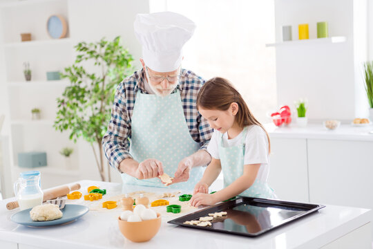 Photo of little pretty girl granddaughter help grandpa chef cap making dough colorful forms putting ready on tray baking cookies cake together free time weekend home kitchen indoors