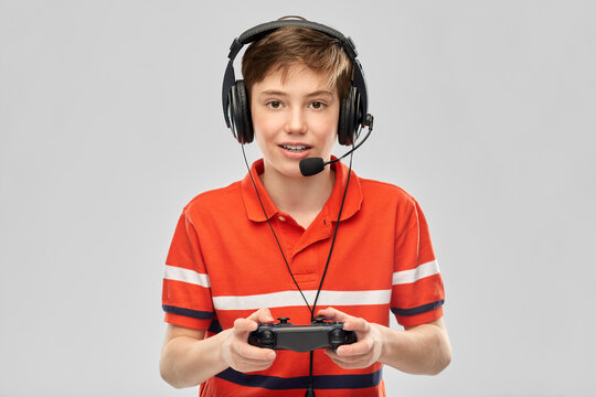 leisure, technology and children concept - smiling boy in headphones with microphone and gamepad playing video game over grey background