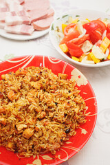 Eastern cuisine. Red plate with pilaf on the table. A plate with salad. Sliced plate of brisket and sausage.