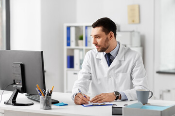 healthcare, medicine and people concept - male doctor with clipboard and computer working at...