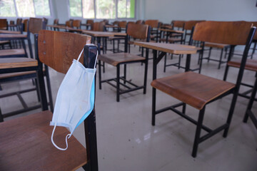 The used medical face mask hang on the wood lecture chairs in the empty classroom. Concept during the Coronavirus disease COVID-19 outbreak and pandemic in the 2020s. Back to school concept.