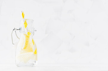 Fresh summer cocktail with sour lemon, soda, straw in yoke bottle on elegant soft light white wooden board and plaster wall.