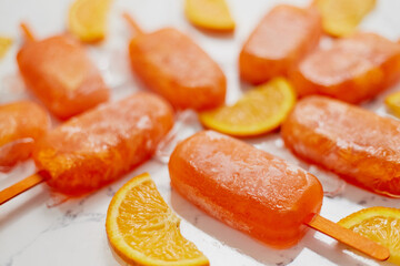 Homemade frozen popsicles made with oragnic fresh oranges placed with ice cubes on marble table