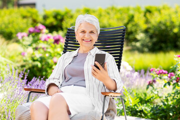 technology, old age and people concept - happy smiling senior woman with smartphone resting at summer garden