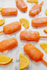 Homemade frozen popsicles made with oragnic fresh oranges placed with ice cubes on marble table