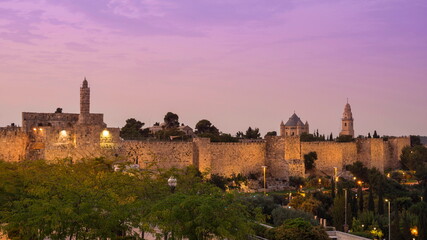 Obraz premium Sunrise view of the Old City wall of Jerusalem, from the mamluk minaret of the Jerusalem Citadel to the Dormition Abbey on Mount Zion, with its lead-covered basilica and a bell tower