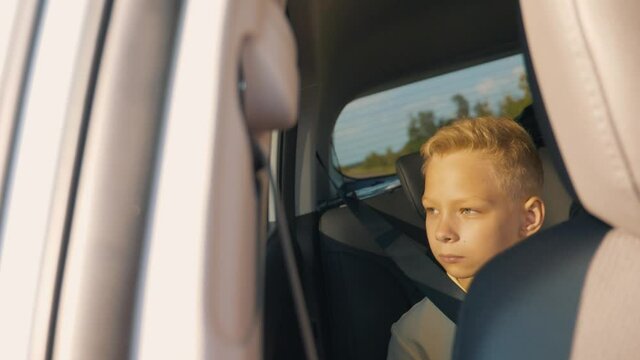 The concept of a family holiday. A school child sits in the back seat of a car and looks out the window enjoying the scenery of the trip. Pensive, dreaming child, sad at the window.