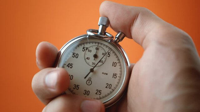 Male hand holding analogue stopwatch on orange color background. Time start with old chronometer man presses start button in the sport concept. Time management concept.