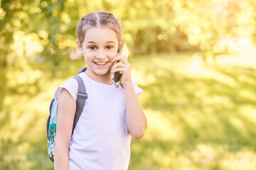 Cute little girl talking. Hold phone near face. Young woman smile. Looking at camera. Outdoor school. Green background. Smiling speach. Happy expression. Student lifestyle