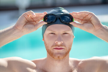Confident man in swimming cap and glasses on head
