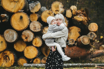 Obraz na płótnie Canvas Happy mother and her little daughter posing against the background of stacked logs on background.