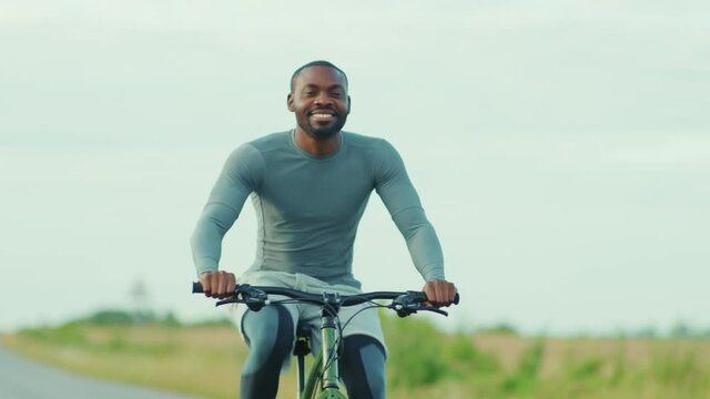 Attractive smiling african american man in cycling on road in the countryside bicycle happy bike biking portrait active raised relax ride sunshine slow motion