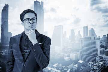 Fototapeta na wymiar Young handsome businessman in suit and glasses dreaming about new career opportunities after MBA graduation. Bangkok on background. Double exposure.